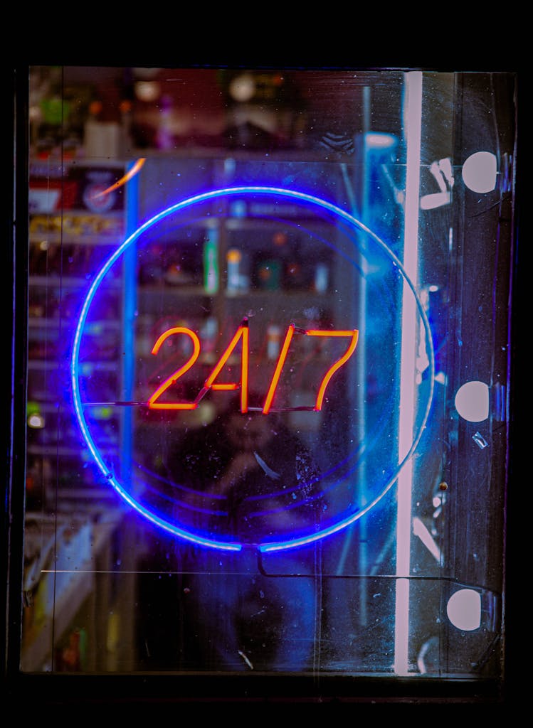 Vibrant neon blue and red 24/7 sign glowing in a shop window at night, creating a bustling urban vibe.